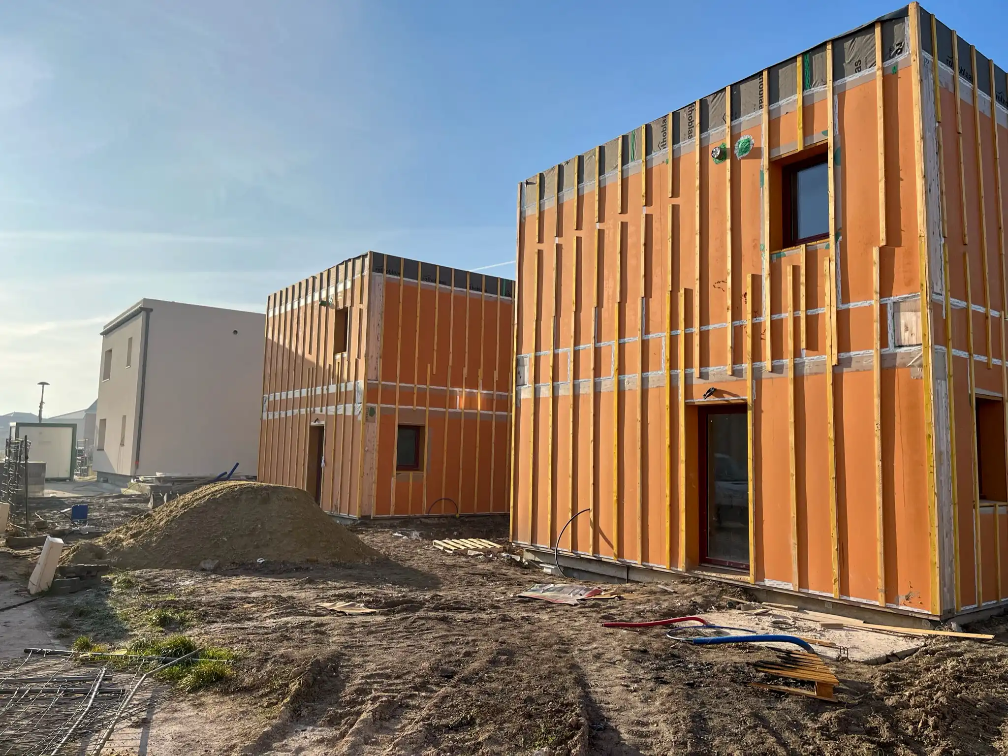 3 maisons au format cubique monté en caissons bois-paille. La maison du fond a déjà été enduite. Les deux autres ont été montés, les menuiseries posés.