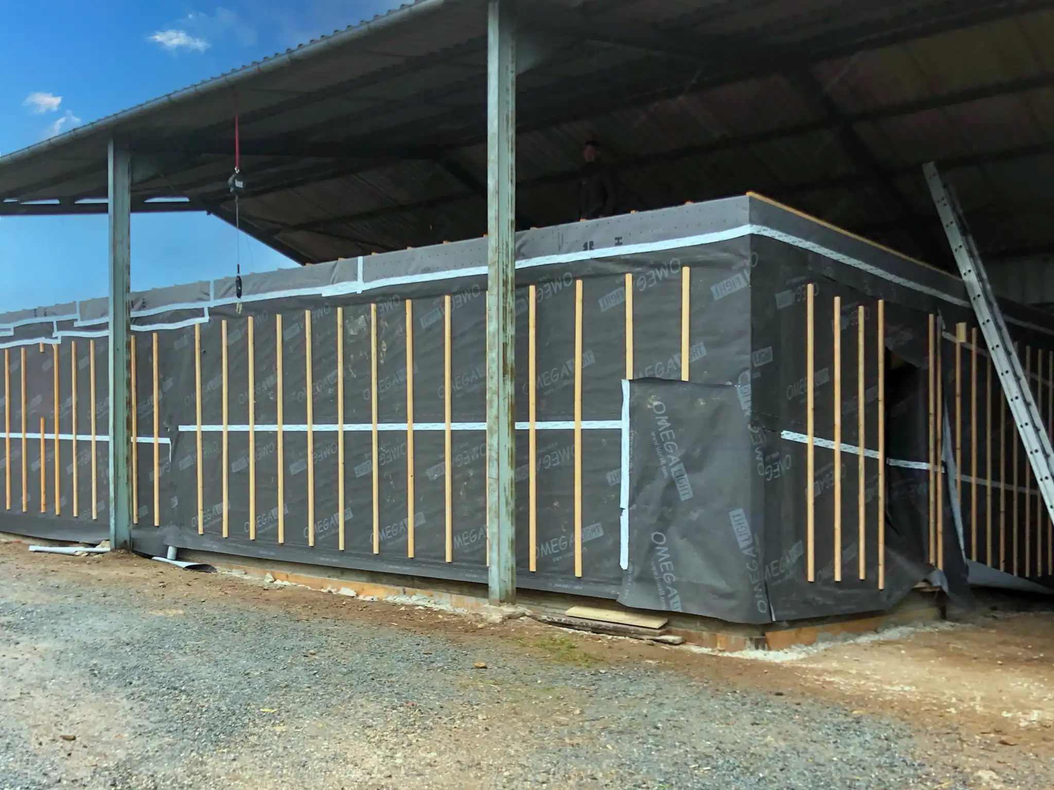 Vue extérieure de cette salle polyvalente construite sous un hangar. Elle est recouverte de pare-pluie.